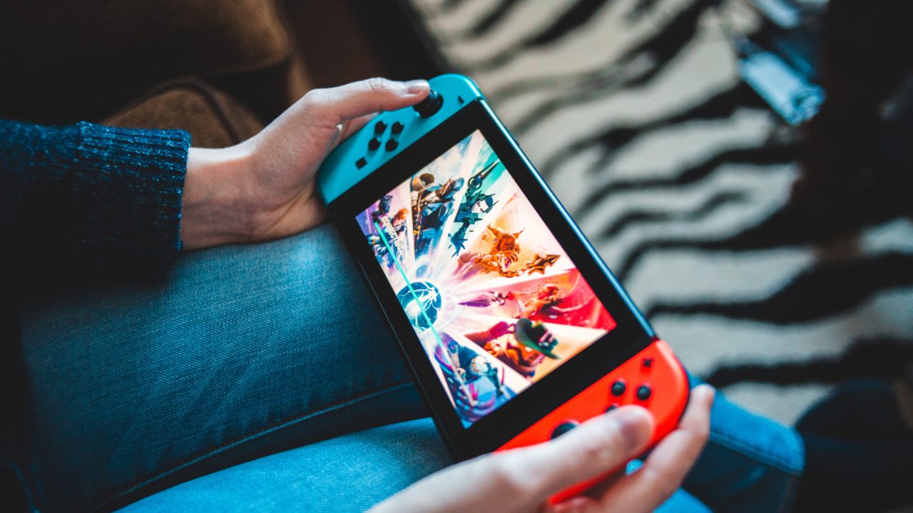 Une personne tient une console Nintendo Switch dans ses mains et joue à un jeu vidéo.
