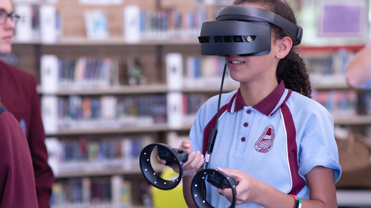 Une jeune femme porte un casque de réalité virtuelle et tient les manettes dans ses mains.